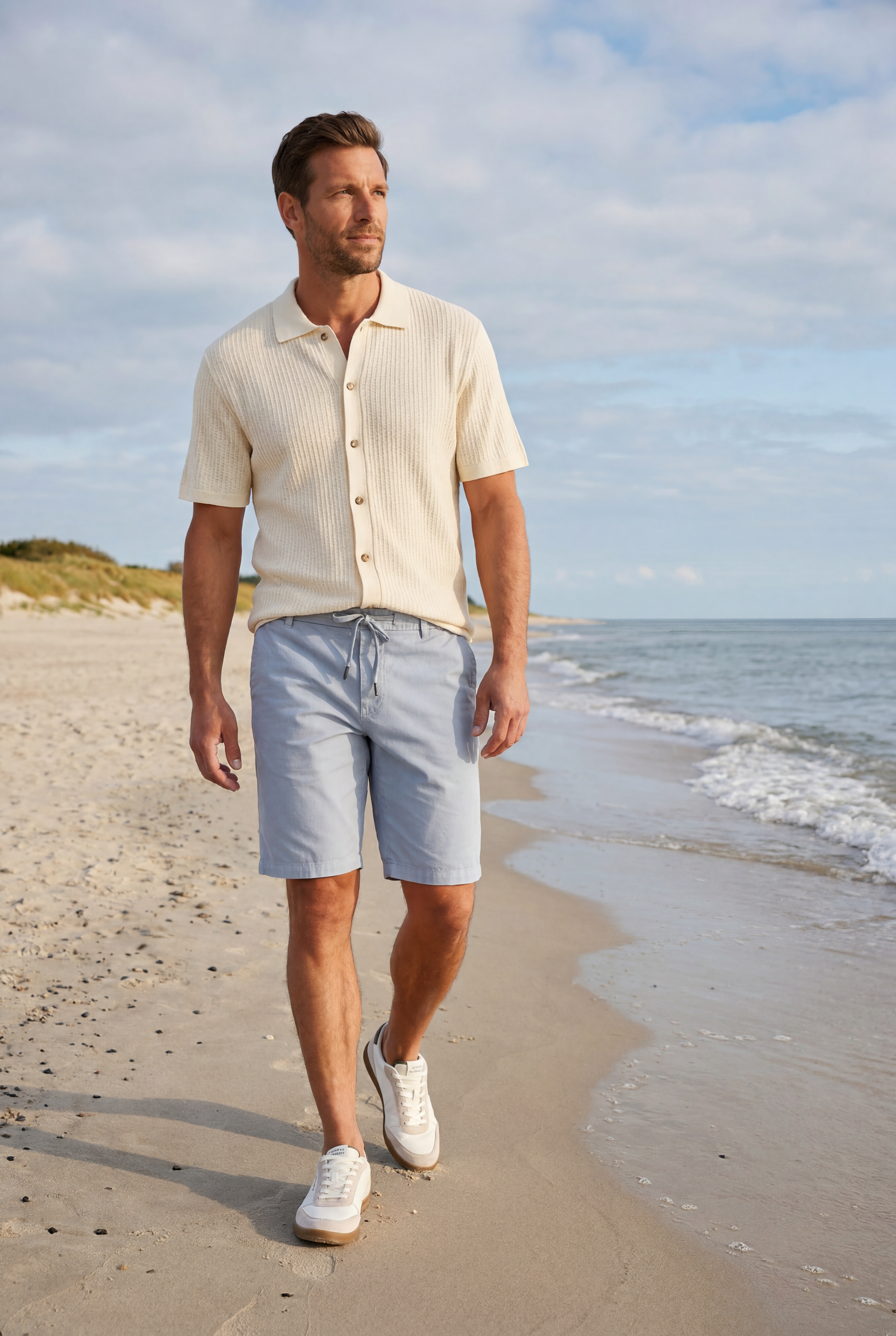 Mann trägt ecru Pointelle Strick-Polo von Les Deux und blaue Shorts am Strand - Pier 14