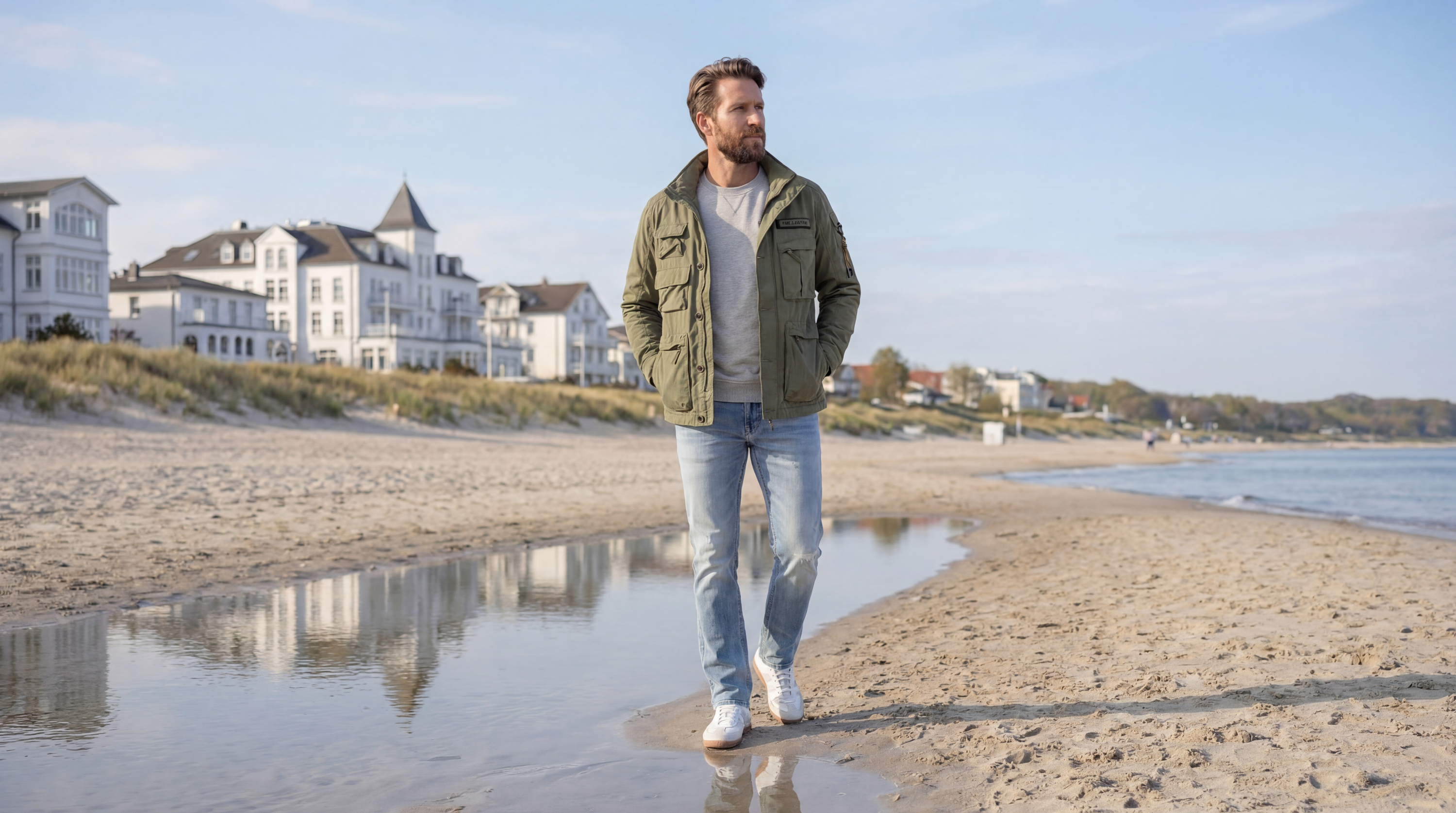 Mann trägt olivgrüne PME Legend Jacke, grauen Pullover und Jeans am Strand - Frühlingsbasics für Herren bei Pier 14