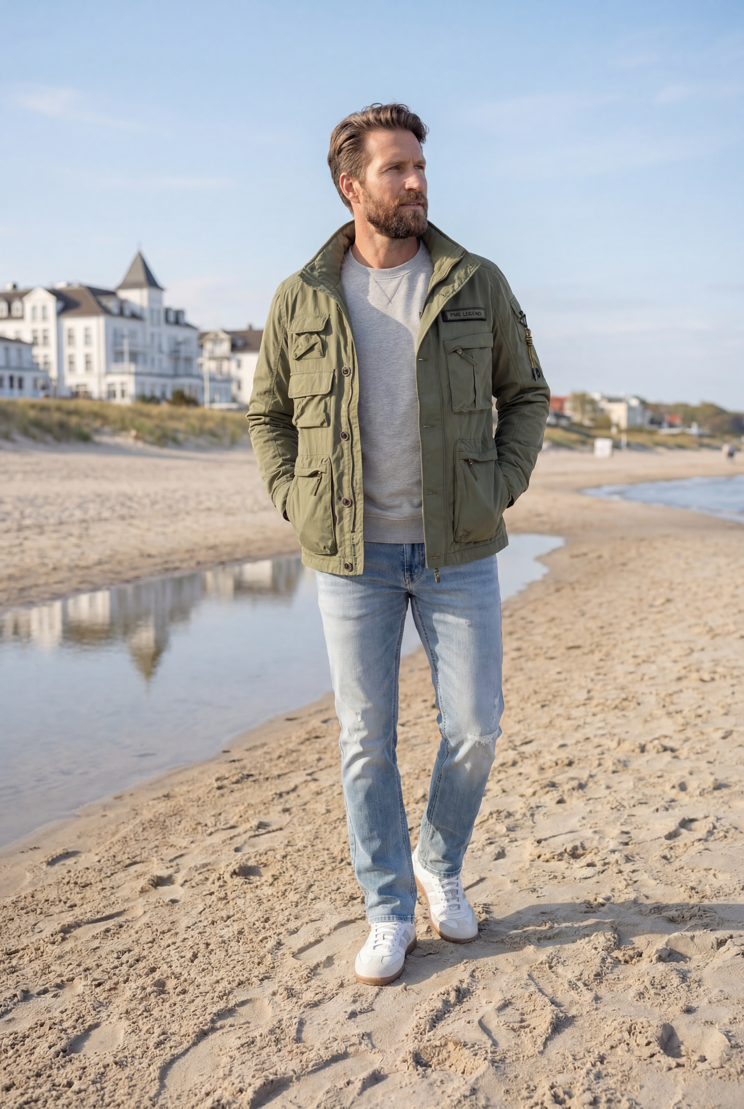 Mann trägt olivgrüne PME Legend Jacke, grauen Pullover und Jeans am Strand - Frühlingsbasics für Herren bei Pier 14